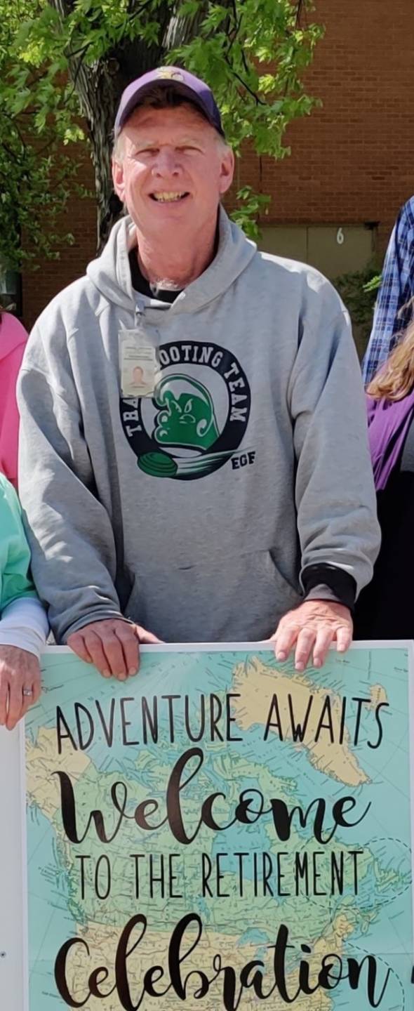 Greg smiles as he holds a "welcome to retirement" sign for a colleague outside the NDVS/SB building.